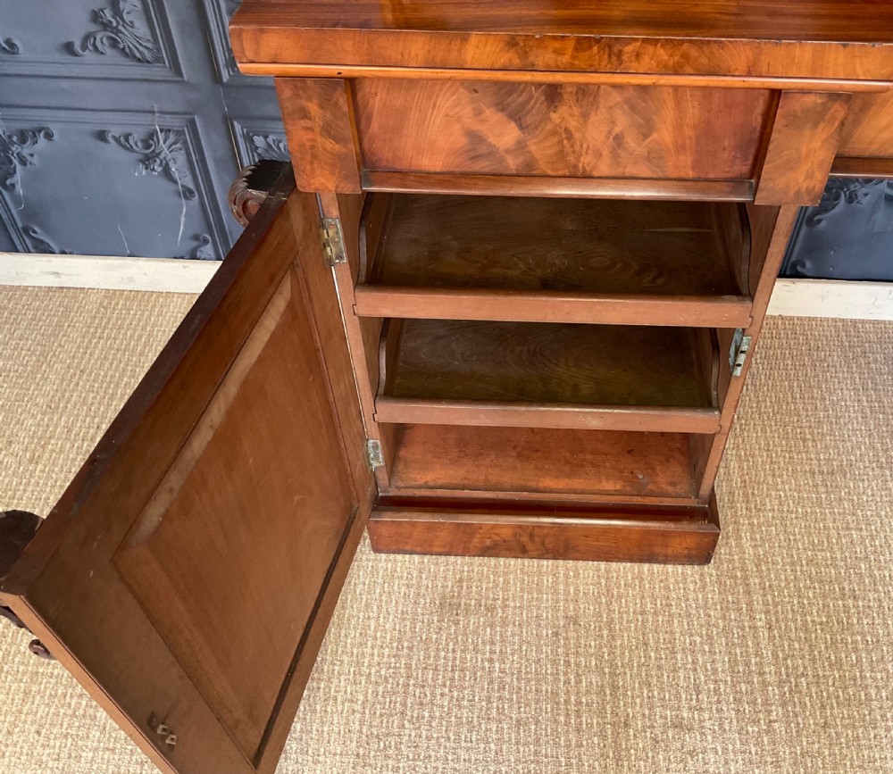 A Victorian mahogany pedestal sideboard featuring a carved arched backboard, flame mahogany veneer panels, and twin pedestal cupboards. View XI