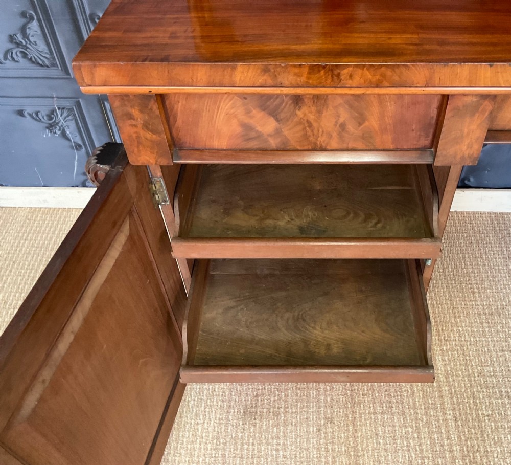 A Victorian mahogany pedestal sideboard featuring a carved arched backboard, flame mahogany veneer panels, and twin pedestal cupboards. View XII