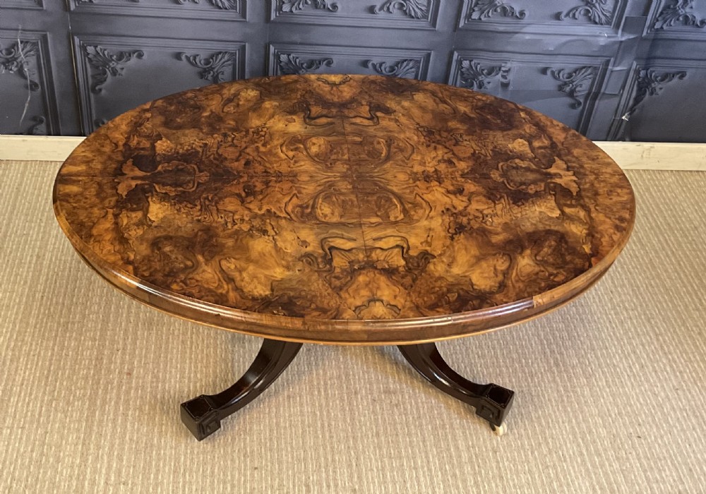 An oval Victorian low coffee table featuring a bookmatched burr walnut veneer top supported by dark curved legs on small castors. View II