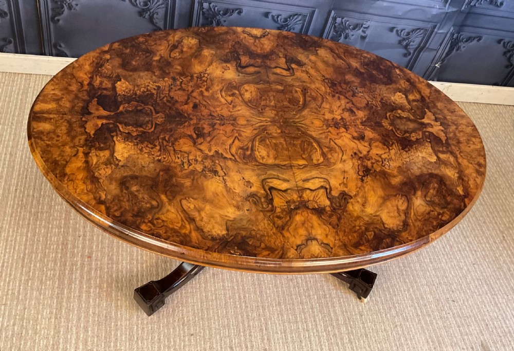 An oval Victorian low coffee table featuring a bookmatched burr walnut veneer top supported by dark curved legs on small castors. View V