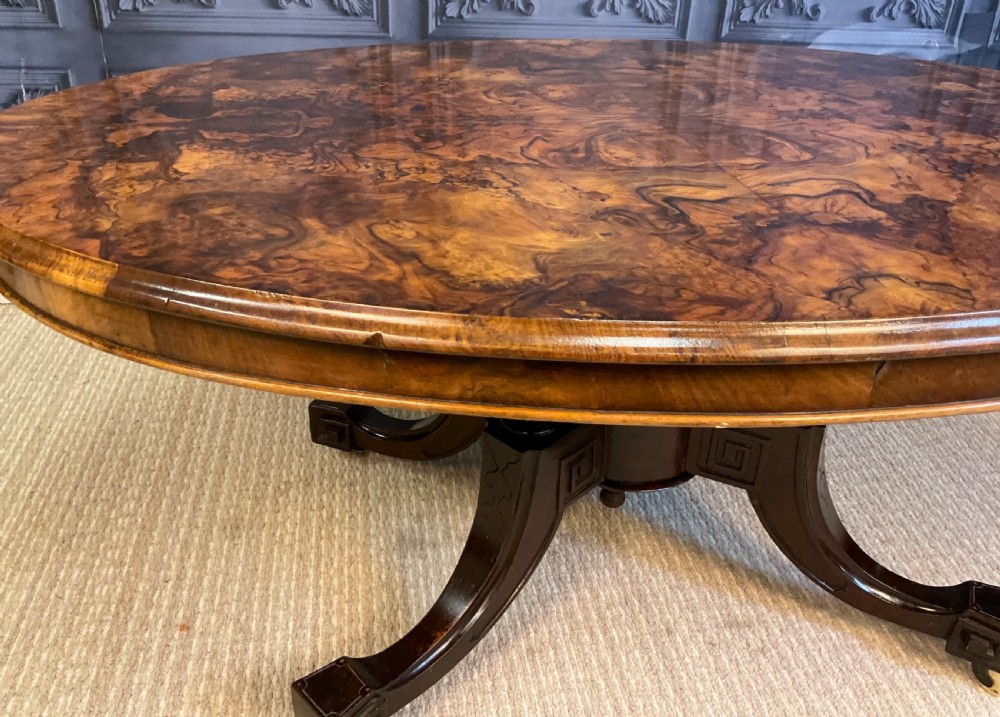 An oval Victorian low coffee table featuring a bookmatched burr walnut veneer top supported by dark curved legs on small castors. View VII