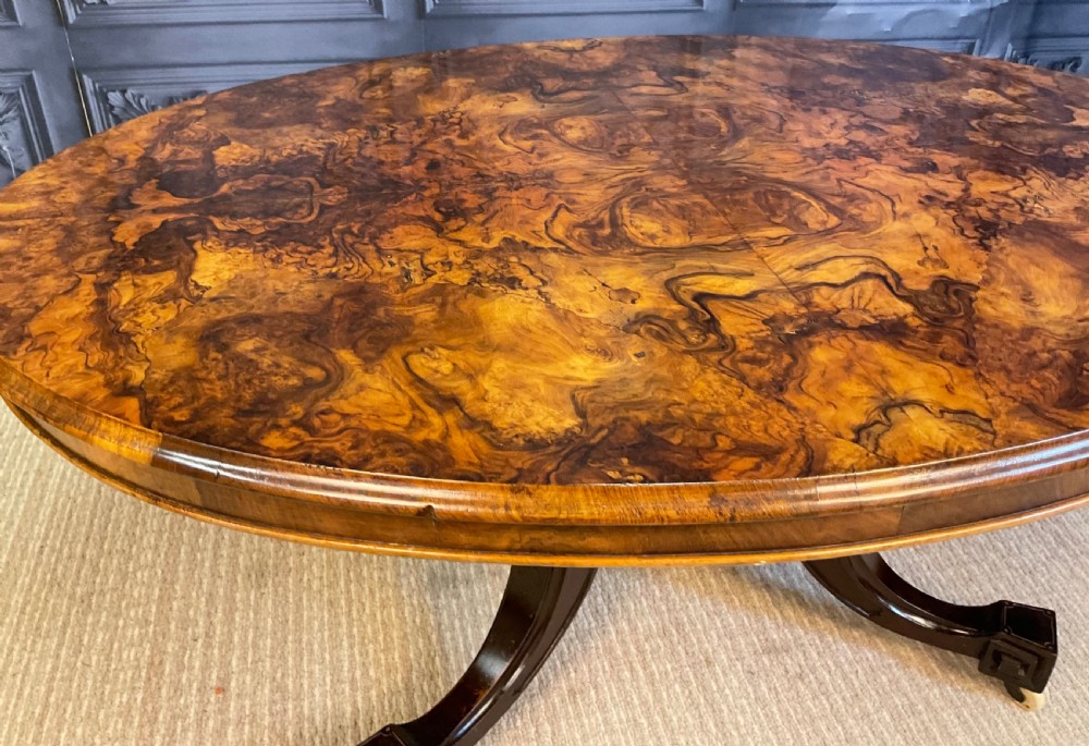 An oval Victorian low coffee table featuring a bookmatched burr walnut veneer top supported by dark curved legs on small castors. View VIII