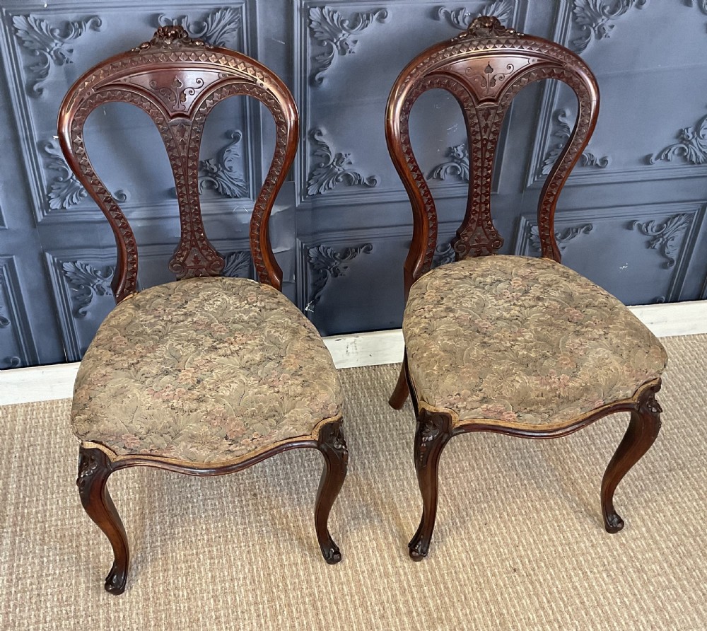 A pair of Victorian carved dark wood side chairs featuring open-work balloon backs, patterned tapestry upholstered seats, and cabriole legs.