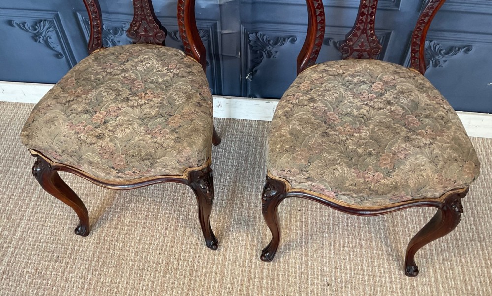 A pair of Victorian carved dark wood side chairs featuring open-work balloon backs, patterned tapestry upholstered seats, and cabriole legs. View V