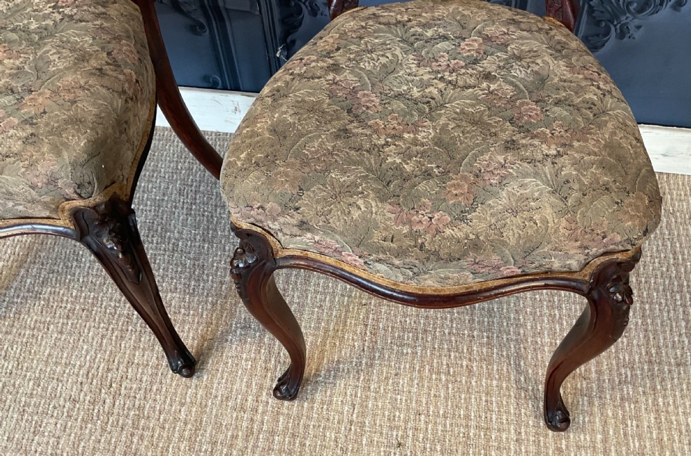 A pair of Victorian carved dark wood side chairs featuring open-work balloon backs, patterned tapestry upholstered seats, and cabriole legs. View VI