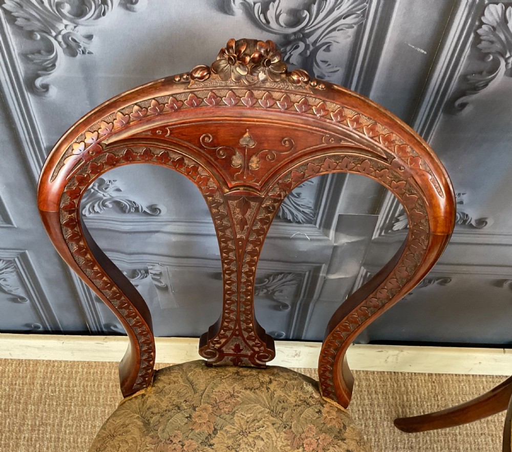 A pair of Victorian carved dark wood side chairs featuring open-work balloon backs, patterned tapestry upholstered seats, and cabriole legs. View X