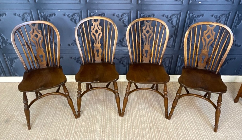 A set of four warm brown wooden Windsor style dining chairs with hoop backs, pierced central splats, and turned legs.