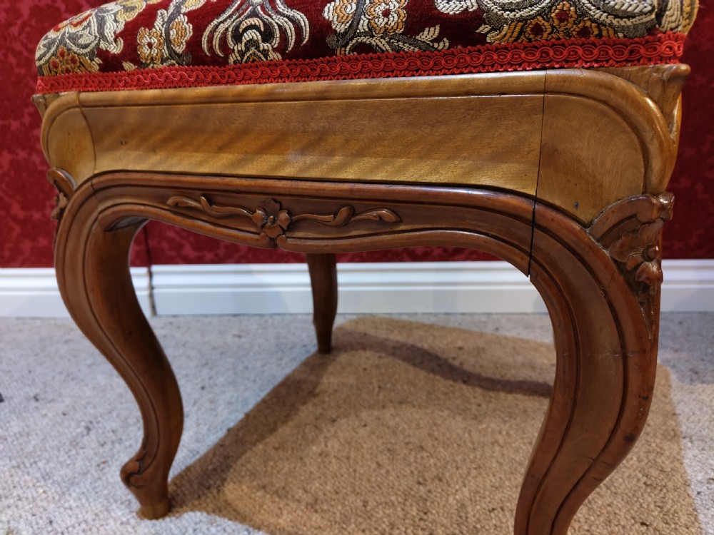 An antique carved walnut piano stool with cabriole legs and a red floral tapestry upholstered top. View V