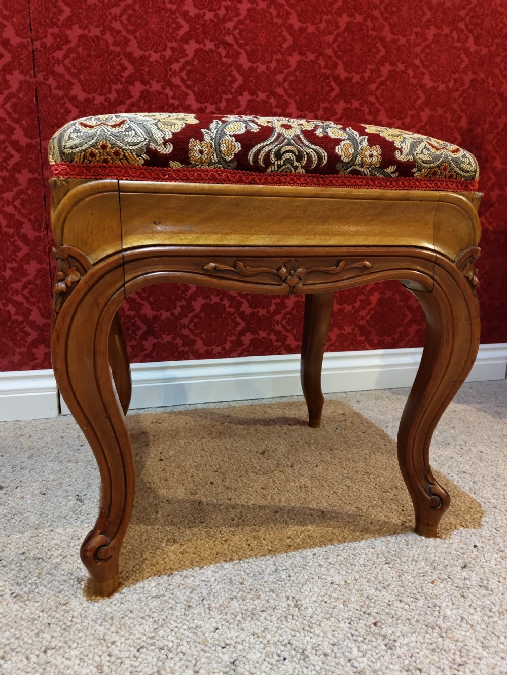 An antique carved walnut piano stool with cabriole legs and a red floral tapestry upholstered top.