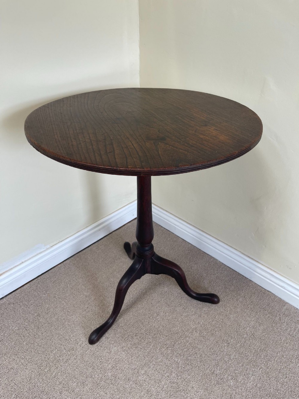 An antique dark wood wine table featuring a circular top mounted on a turned central pedestal with three splayed legs.