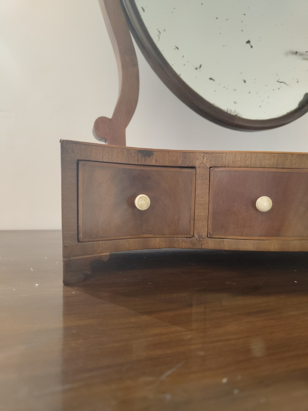 An antique mahogany dressing table mirror with an oval swivelling glass plate set above a serpentine base with small drawers. View II