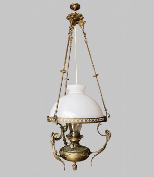 fig 1. A late Victorian brass hanging lamp featuring a white opaline glass shade, decorative rams head side scrolls, and a central burner unit.