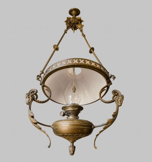 fig 2. A late Victorian brass hanging lamp featuring a white opaline glass shade, decorative rams head side scrolls, and a central burner unit.