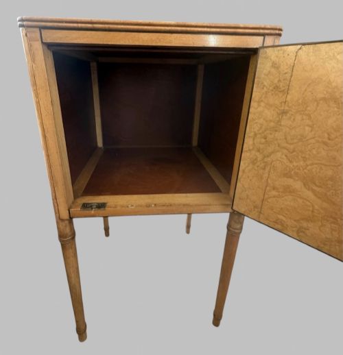 fig 1. An Art Deco burr walnut bedside cabinet with a single door, circular brass handle, geometric inlaid top, and four slender tapered legs.