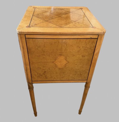 fig 2. An Art Deco burr walnut bedside cabinet with a single door, circular brass handle, geometric inlaid top, and four slender tapered legs.
