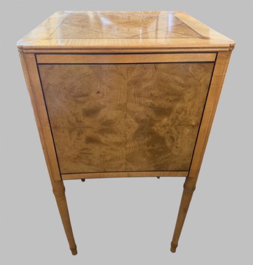 fig 3. An Art Deco burr walnut bedside cabinet with a single door, circular brass handle, geometric inlaid top, and four slender tapered legs.