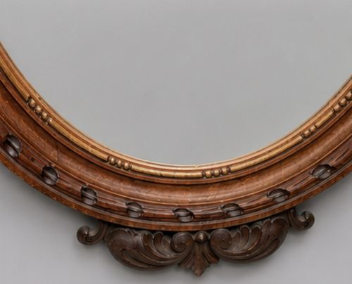 fig 2. A late 19th-century oval wall mirror featuring a carved wooden frame topped with a sculpted ribbon cresting and floral motifs.