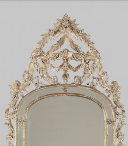 fig 1. An antique nineteenth-century French giltwood mirror featuring elaborate carved cresting with foliage motifs and an arched frame.