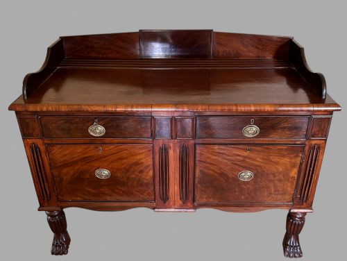 fig 1. A 19th-century flame mahogany sideboard featuring two upper drawers, two cabinet doors, reeded pilasters, oval brass handles, a low gallery back, and carved paw feet.