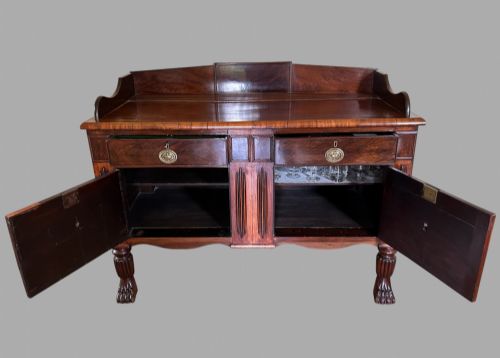 fig 3. A 19th-century flame mahogany sideboard featuring two upper drawers, two cabinet doors, reeded pilasters, oval brass handles, a low gallery back, and carved paw feet.