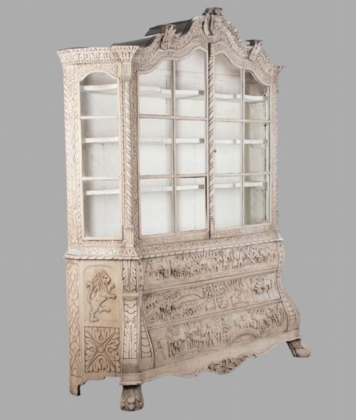 fig 2. A tall nineteenth-century Dutch carved pale oak display cabinet featuring a shaped crest, multi-pane glazed upper doors, and a bombe chest base with three relief-carved drawers on paw feet.