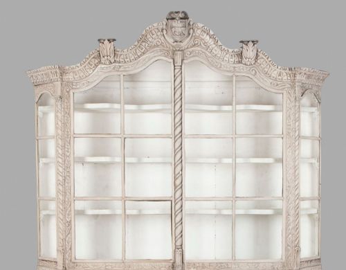 fig 4. A tall nineteenth-century Dutch carved pale oak display cabinet featuring a shaped crest, multi-pane glazed upper doors, and a bombe chest base with three relief-carved drawers on paw feet.