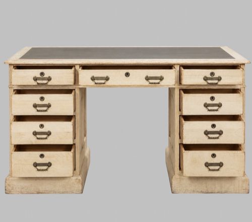 fig 1. A circa 1900 bleached oak pedestal desk featuring nine drawers with brass swing handles and a dark inset leather writing surface.