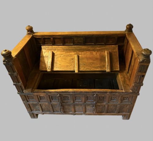 fig 2. A carved dark hardwood storage bench with a hinged lid seat, geometric panelled backrest, corner post finials, and iron fittings.