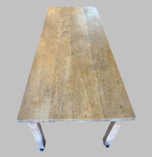 fig 3. A 19th-century rectangular elm farmhouse table featuring a multi-plank top, straight aprons, four square tapering legs, and small metal castors.