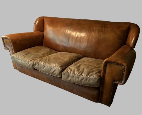 fig 2. A three-seater Art Deco sofa upholstered in warm brown patinated leather with metal studding along the armrests.