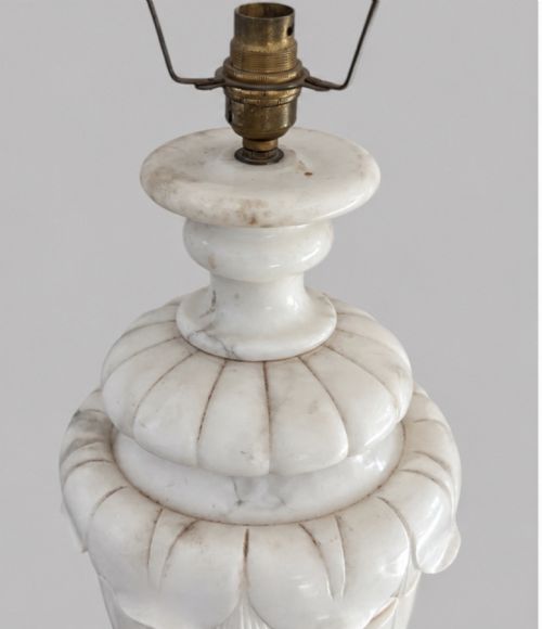 fig 2. A carved off-white alabaster table lamp base shaped like a classical urn with leaf motifs, resting on a stepped square plinth with a brass harp socket.