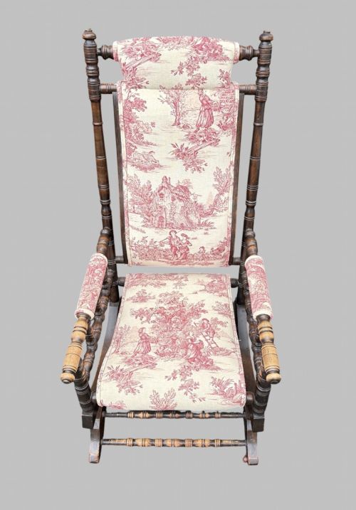 fig 1. An antique turned wood rocking chair featuring dark timber spindle armrests and frame with cream fabric upholstery displaying red figurative pattern work.
