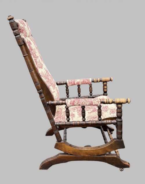 fig 2. An antique turned wood rocking chair featuring dark timber spindle armrests and frame with cream fabric upholstery displaying red figurative pattern work.