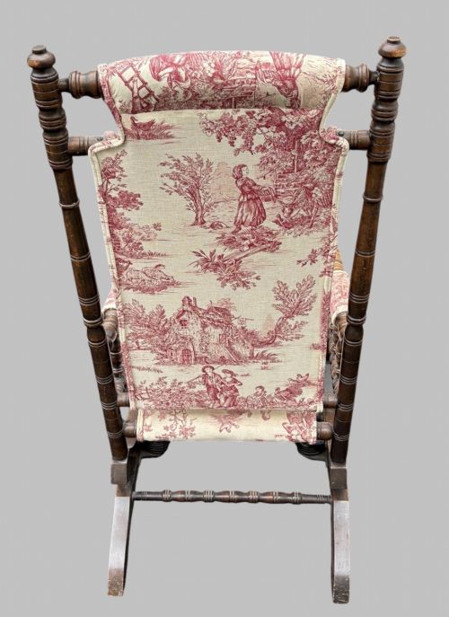 fig 3. An antique turned wood rocking chair featuring dark timber spindle armrests and frame with cream fabric upholstery displaying red figurative pattern work.