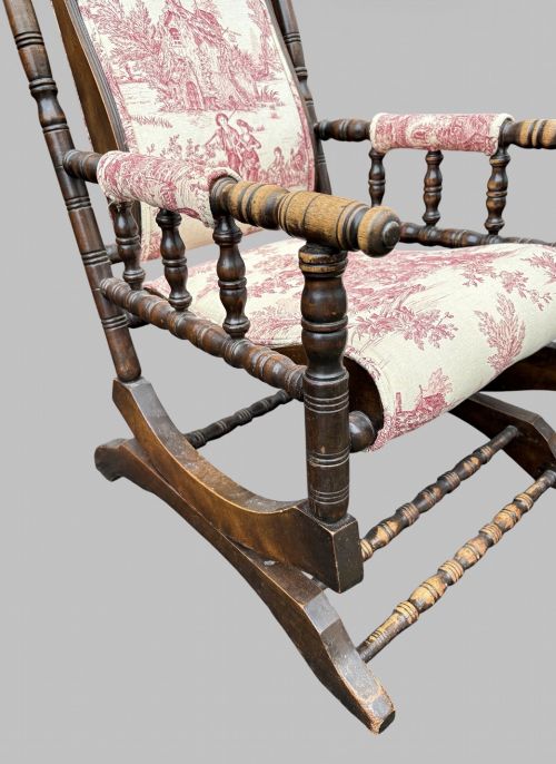 fig 4. An antique turned wood rocking chair featuring dark timber spindle armrests and frame with cream fabric upholstery displaying red figurative pattern work.