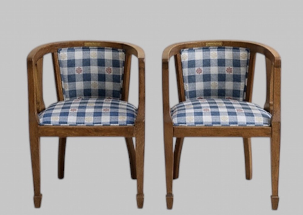 A pair of Arts and Crafts oak tub armchairs with curved wooden frames and blue and white checked fabric upholstery.