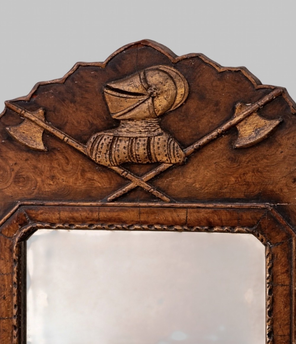 A late nineteenth-century carved walnut wall mirror featuring a scalloped outline, a central rectangular mirror frame, and an armorial crest detailing a knight helmet above crossed battleaxes. View II