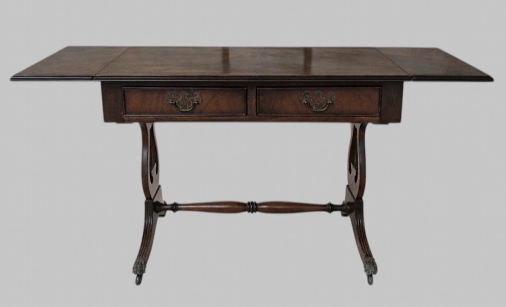 An early 20th-century mahogany drop-leaf table featuring two front drawers with brass swing handles, lyre-shaped end supports, a turned cross-stretcher, and splayed legs on brass castors. View II