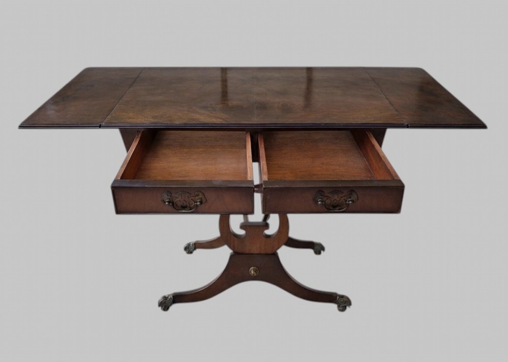 An early 20th-century mahogany drop-leaf table featuring two front drawers with brass swing handles, lyre-shaped end supports, a turned cross-stretcher, and splayed legs on brass castors. View III