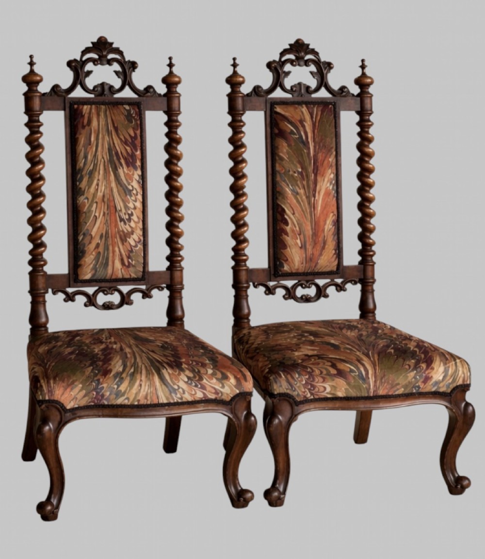 A pair of 19th-century carved walnut hall chairs featuring tall barley twist uprights, ornate cresting, cabriole front legs, and patterned upholstery.