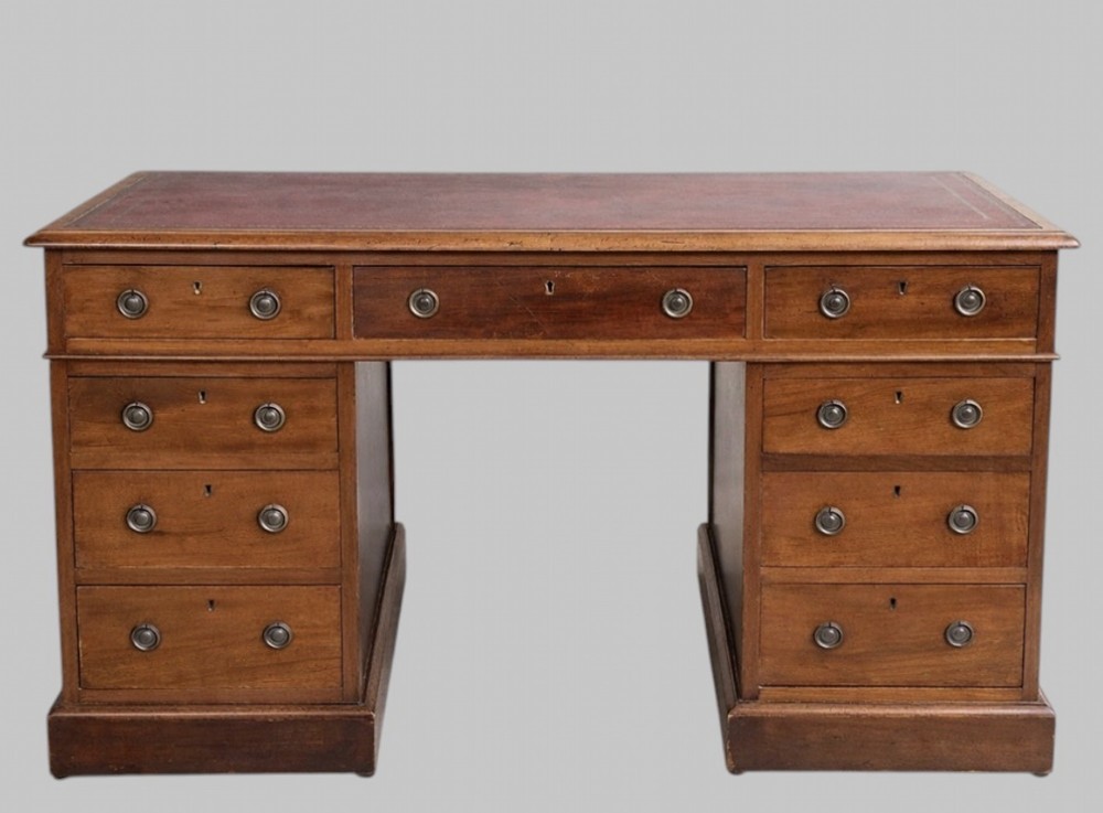 A late Victorian mahogany pedestal desk featuring an inset red leather writing surface, nine drawers with round brass pulls, and two plinth bases.