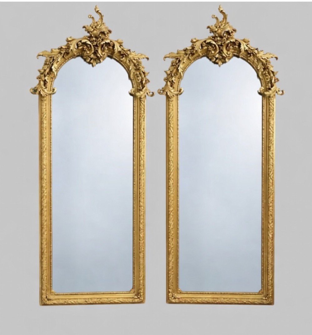 A pair of tall arched giltwood mirrors featuring detailed acanthus leaf cresting and moulded gold frames.