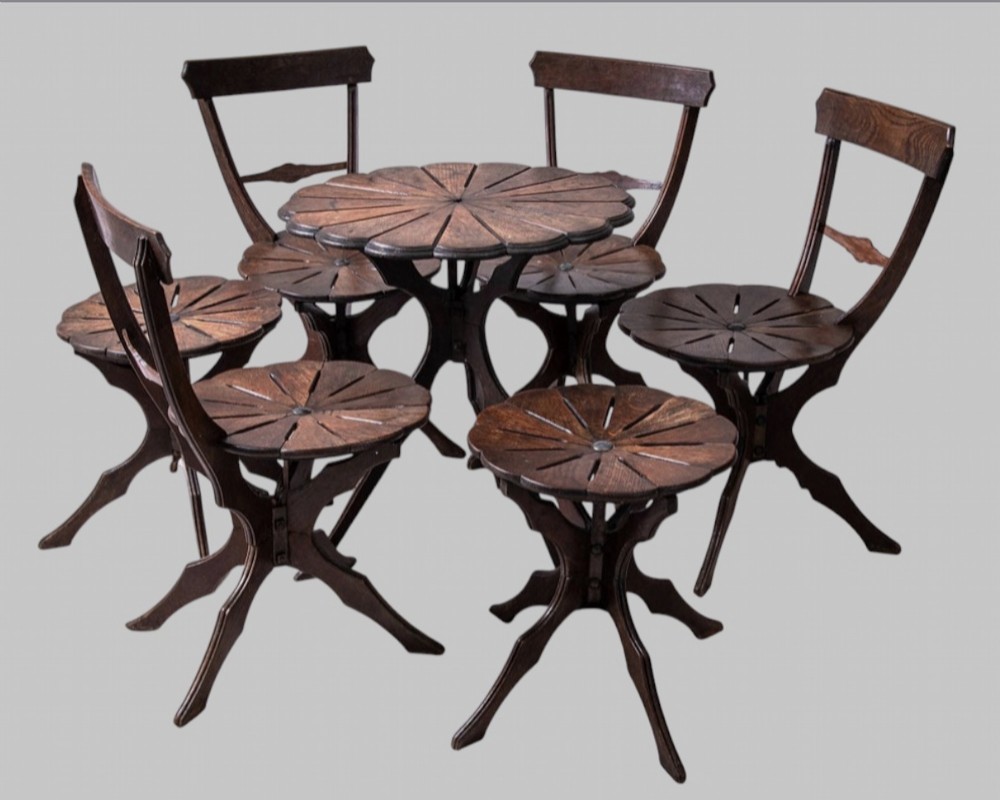 A seven-piece dark carved oak parlour suite comprising a central round table, five chairs, and one stool with radiating petal design tops and curved trestle legs.