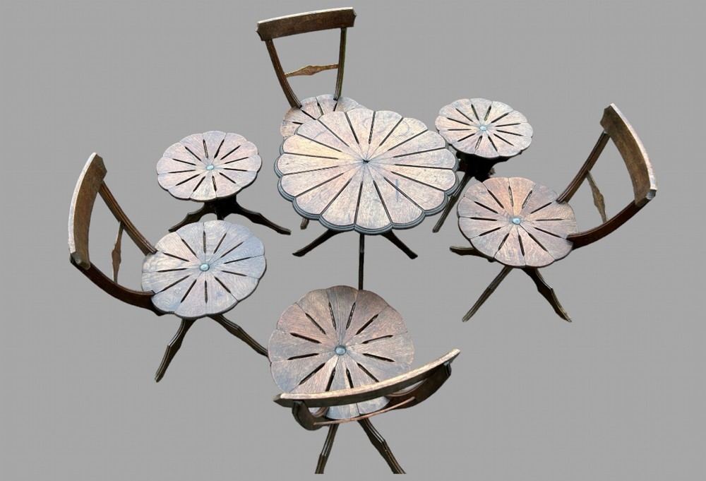 A seven-piece dark carved oak parlour suite comprising a central round table, five chairs, and one stool with radiating petal design tops and curved trestle legs. View II