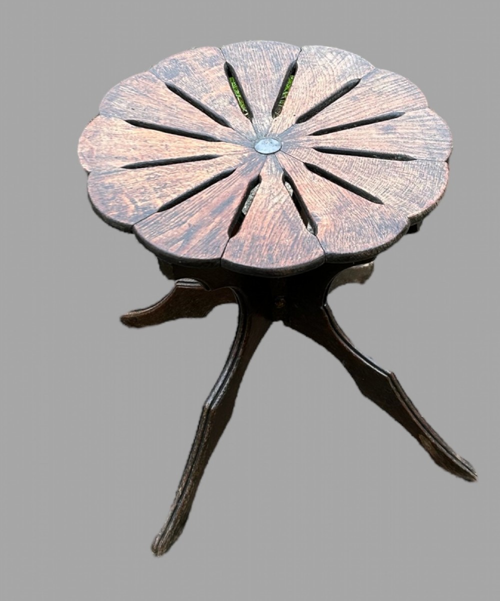A seven-piece dark carved oak parlour suite comprising a central round table, five chairs, and one stool with radiating petal design tops and curved trestle legs. View VI