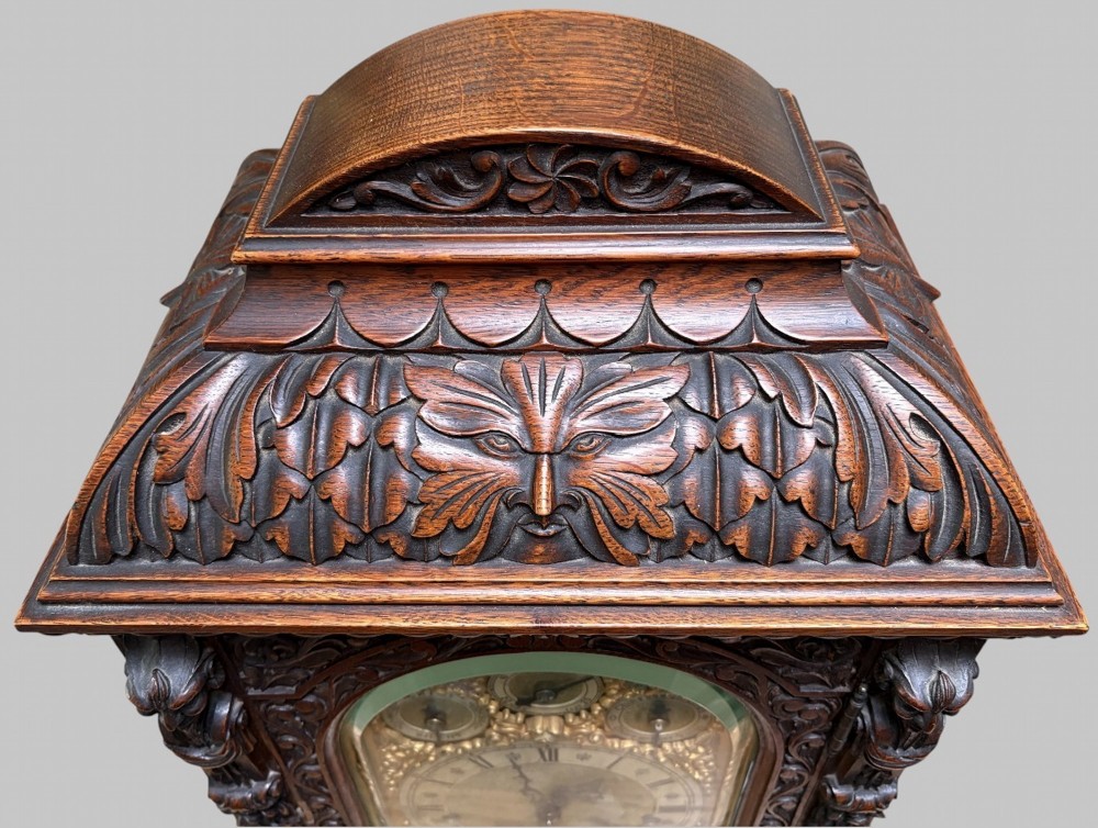 An intricately carved dark oak bracket clock featuring an arched brass dial, corner mask carvings, and foliate cresting. View IV