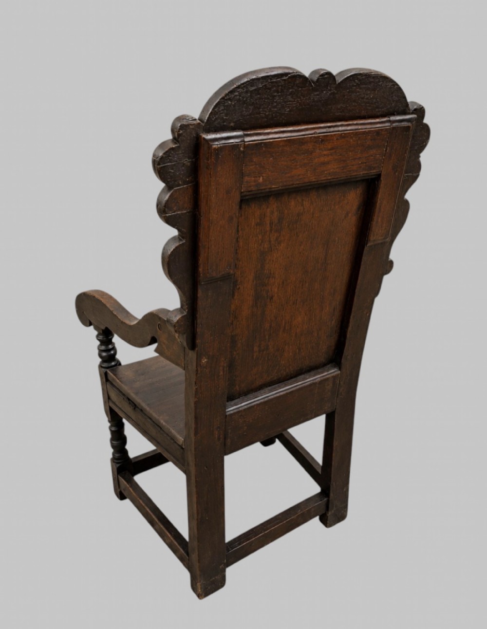 A dark carved oak wainscot armchair featuring a detailed cresting rail, central lozenge panel back, curved arms, and turned front legs. View IV