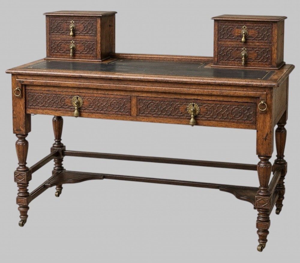 Victorian carved oak writing desk featuring a leather inset surface, two raised drawer cabinets on the top, two carved frieze drawers with brass drop handles, turned legs, and stretchers.