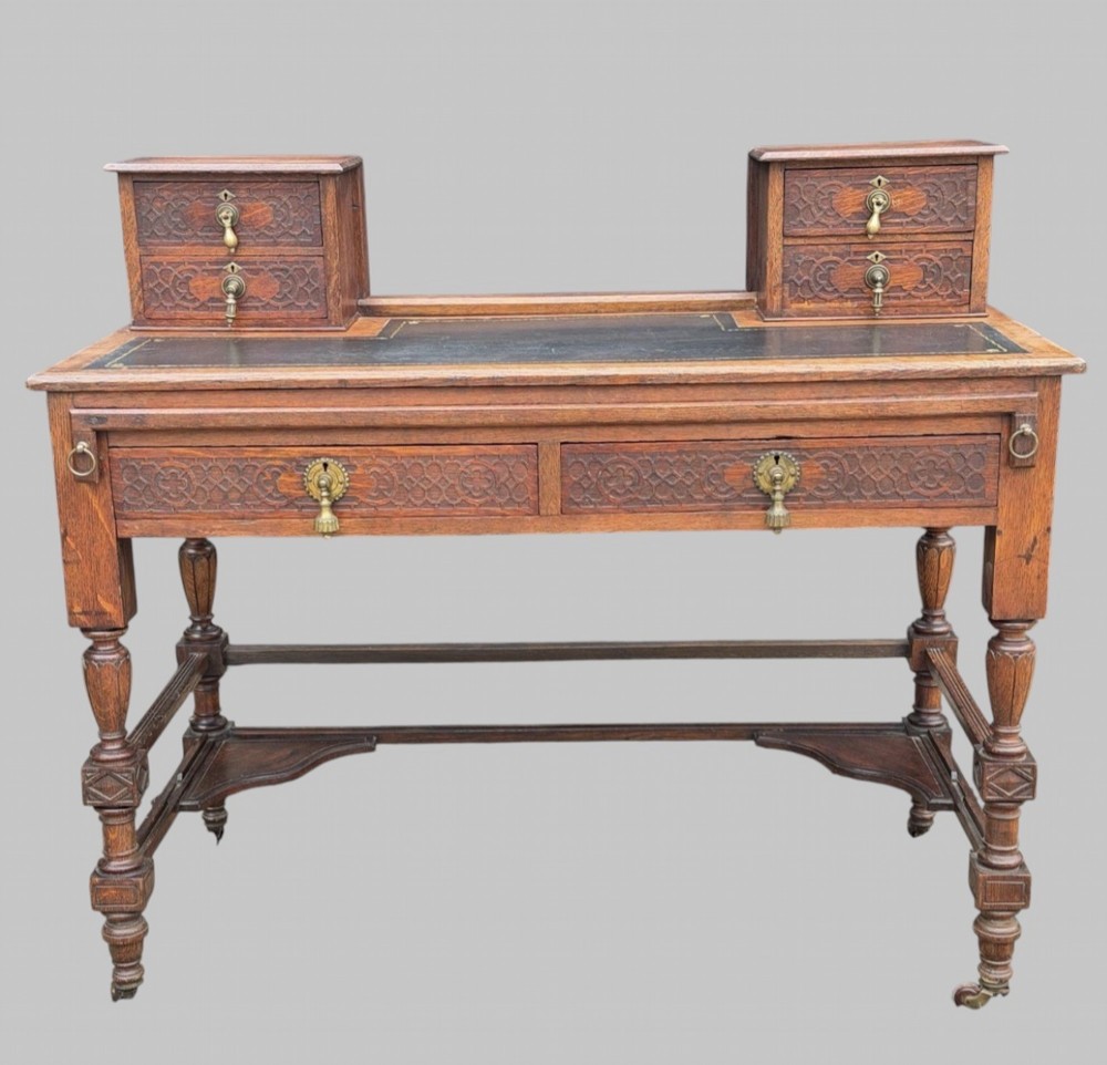 Victorian carved oak writing desk featuring a leather inset surface, two raised drawer cabinets on the top, two carved frieze drawers with brass drop handles, turned legs, and stretchers. View II