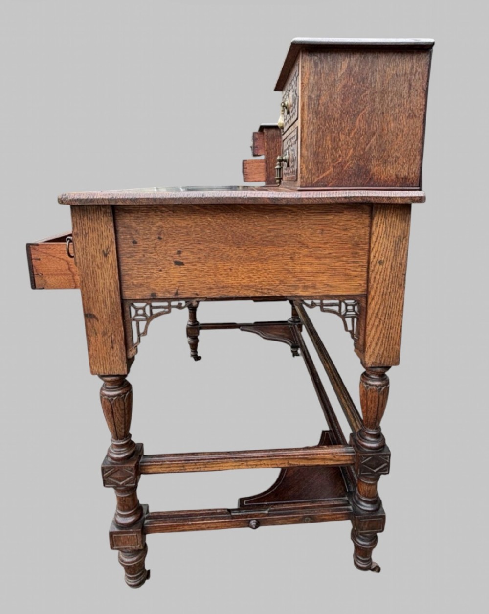 Victorian carved oak writing desk featuring a leather inset surface, two raised drawer cabinets on the top, two carved frieze drawers with brass drop handles, turned legs, and stretchers. View III